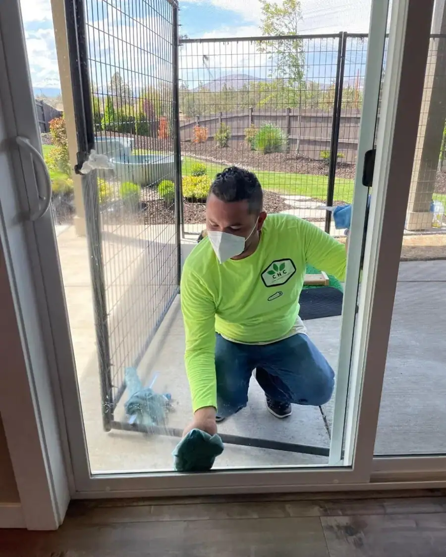 A Central Natural Cleaning crew member in a green CNC shirt cleaning a sliding glass door track