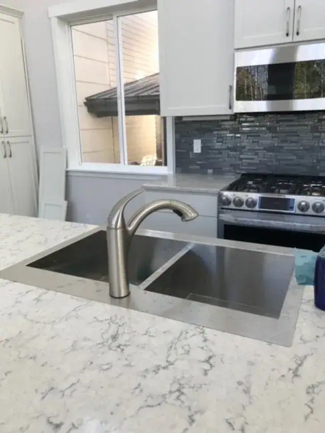 A clean stainless kitchen sink and quartz counter after a house cleaning