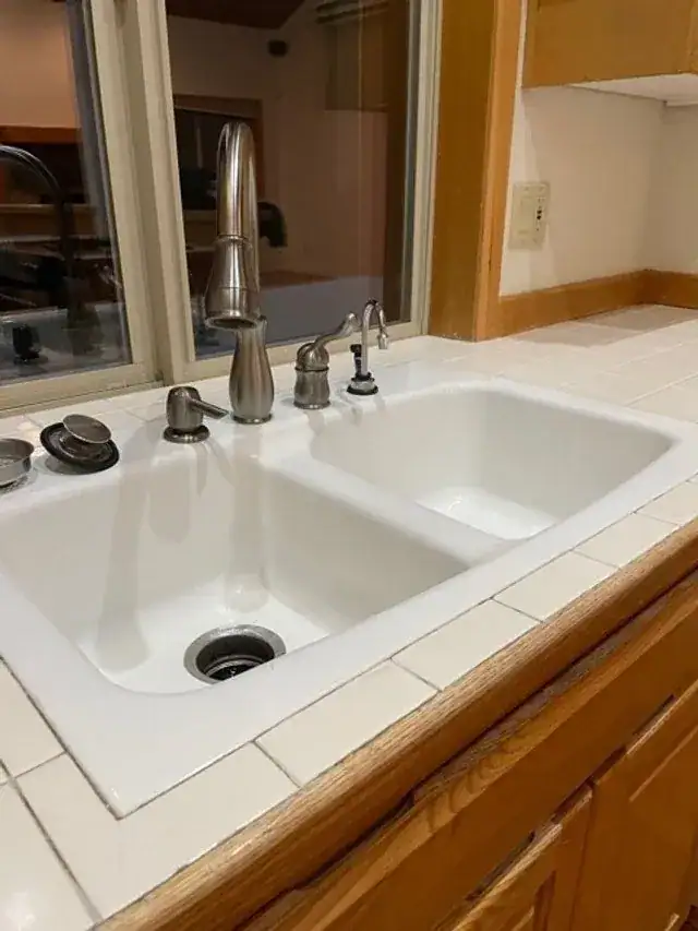 A clean white double sink in a tiled counter