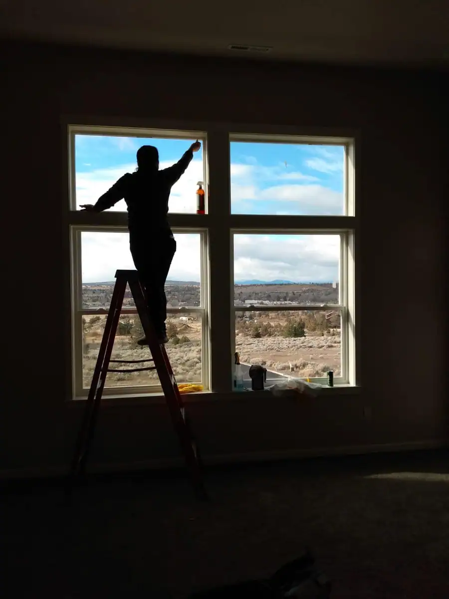A Central Natural Cleaning crew member on a ladder cleaning tall interior windows over the high desert